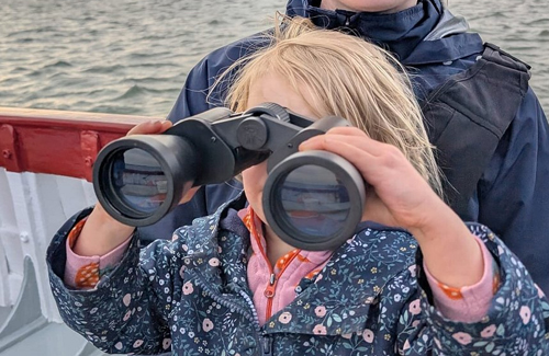 Young girl on Bishops Boat looking through binoculars.
